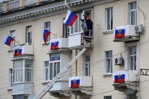 Работници окачват руски знамена на жилищна сграда в Луганск, Украйна, във вторник, 27 септември. (AP Photo)